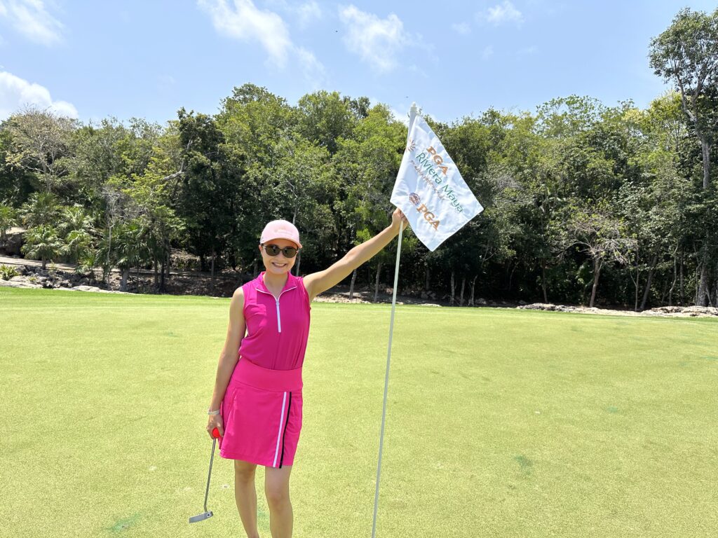 Woman in pink golf outfit holding a flag on a golf course.